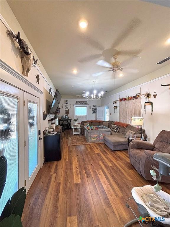 living area with visible vents, wood finished floors, and ceiling fan with notable chandelier