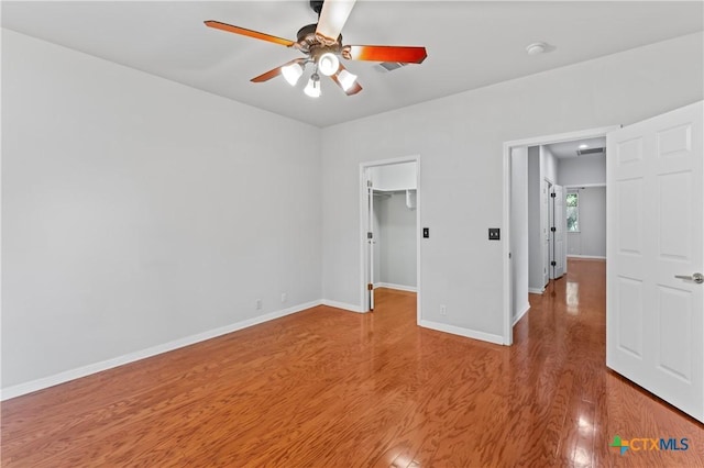 unfurnished bedroom featuring hardwood / wood-style floors, a walk in closet, a closet, and ceiling fan