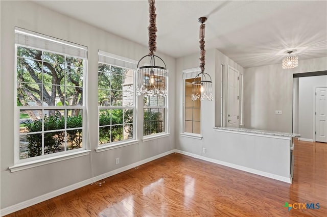 unfurnished dining area with wood-type flooring and an inviting chandelier