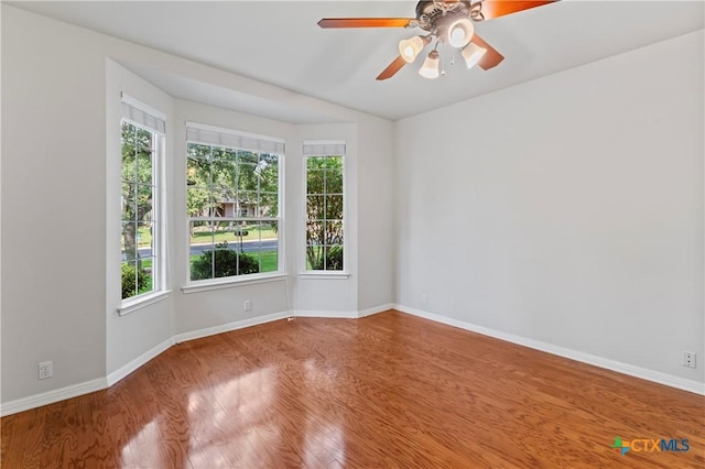 empty room with ceiling fan, plenty of natural light, and hardwood / wood-style floors