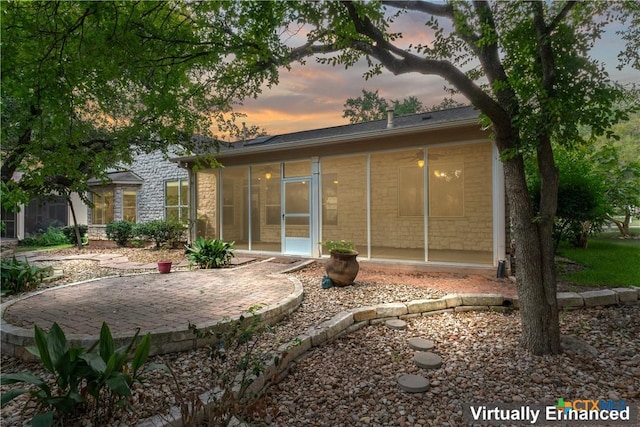 back house at dusk featuring a sunroom and a patio area