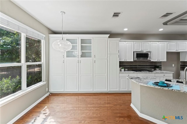 kitchen featuring tasteful backsplash, light stone counters, white cabinetry, and hanging light fixtures