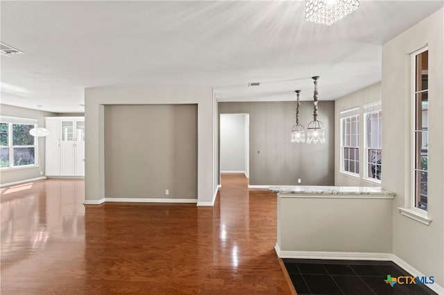 interior space featuring a chandelier, decorative light fixtures, light stone counters, and dark wood-type flooring