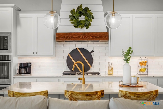 kitchen with appliances with stainless steel finishes, pendant lighting, white cabinetry, and tasteful backsplash