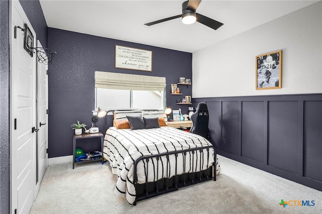 carpeted bedroom featuring a wainscoted wall, ceiling fan, and a decorative wall