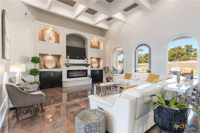 living room featuring a towering ceiling, marble finish floor, coffered ceiling, and a glass covered fireplace