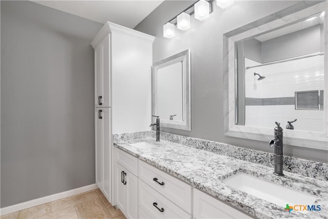 full bathroom featuring double vanity, tiled shower, a sink, and baseboards