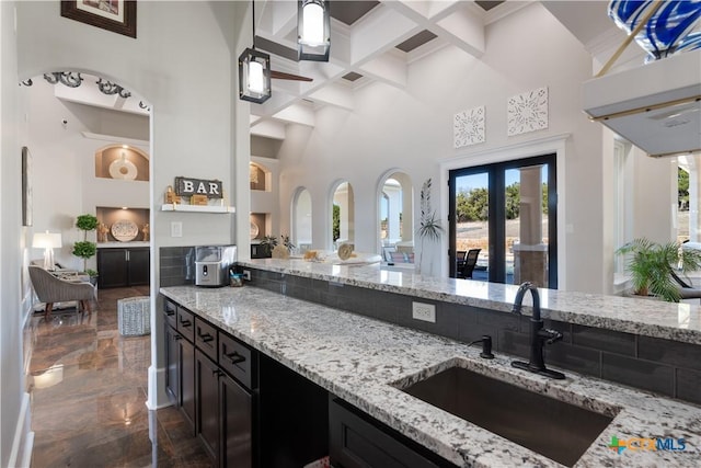 kitchen with marble finish floor, light stone counters, coffered ceiling, and a sink