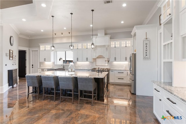 kitchen with crown molding, a breakfast bar area, freestanding refrigerator, white cabinets, and a large island with sink