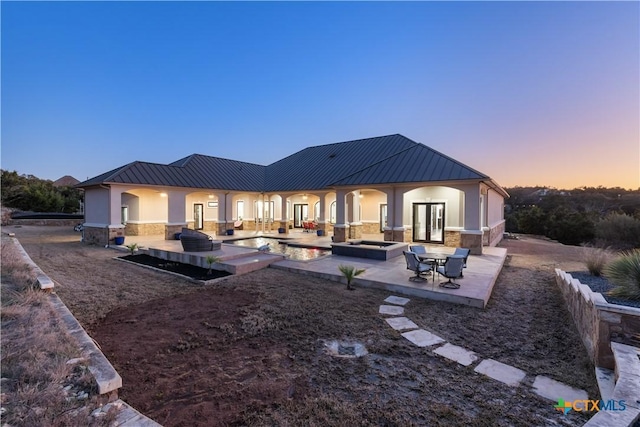 back of property at dusk with stone siding, a standing seam roof, a patio, and stucco siding