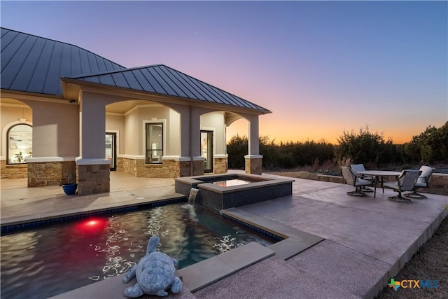 pool at dusk featuring a patio area, an outdoor pool, and an in ground hot tub