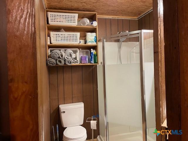 bathroom with wooden walls, an enclosed shower, and toilet