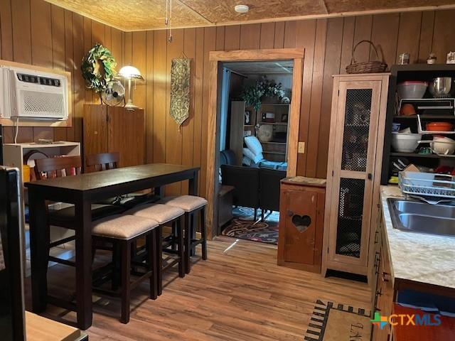 dining space with light wood-type flooring, a wall mounted AC, wooden walls, and sink