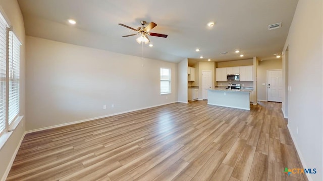 unfurnished living room featuring light wood-type flooring, baseboards, visible vents, and ceiling fan