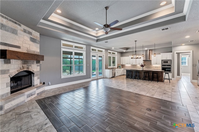 unfurnished living room featuring ceiling fan, a stone fireplace, a textured ceiling, and a tray ceiling