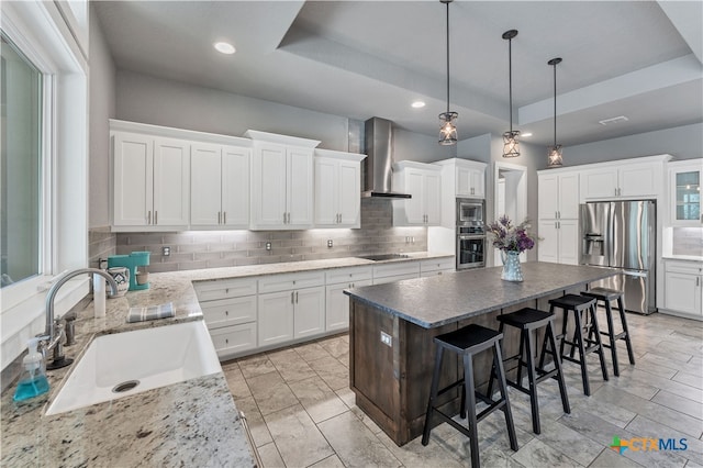 kitchen with wall chimney range hood, white cabinets, sink, and stainless steel appliances