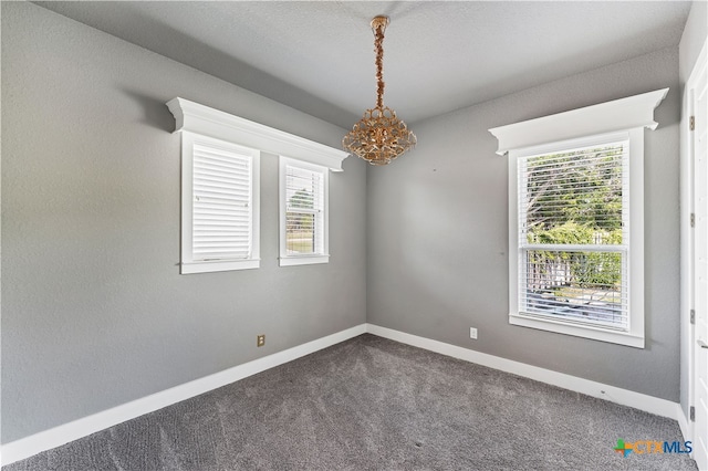 carpeted empty room with a textured ceiling and a notable chandelier