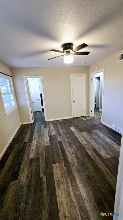 unfurnished living room featuring baseboards, visible vents, dark wood finished floors, and a textured ceiling