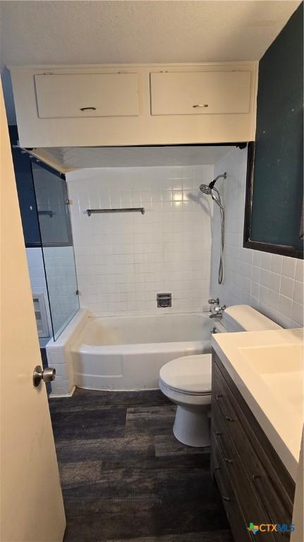 bathroom with toilet, wood finished floors,  shower combination, vanity, and tile walls