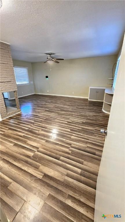 unfurnished living room featuring baseboards, a ceiling fan, wood finished floors, a textured ceiling, and a brick fireplace