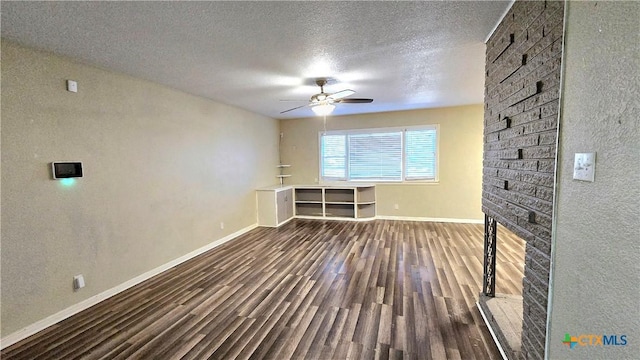 unfurnished living room featuring a ceiling fan, a brick fireplace, a textured ceiling, wood finished floors, and baseboards