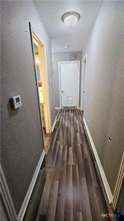 hallway featuring dark wood-type flooring, visible vents, a textured wall, and baseboards