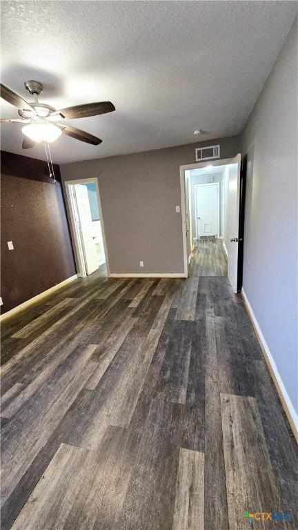 empty room with dark wood-type flooring, visible vents, a textured ceiling, and baseboards