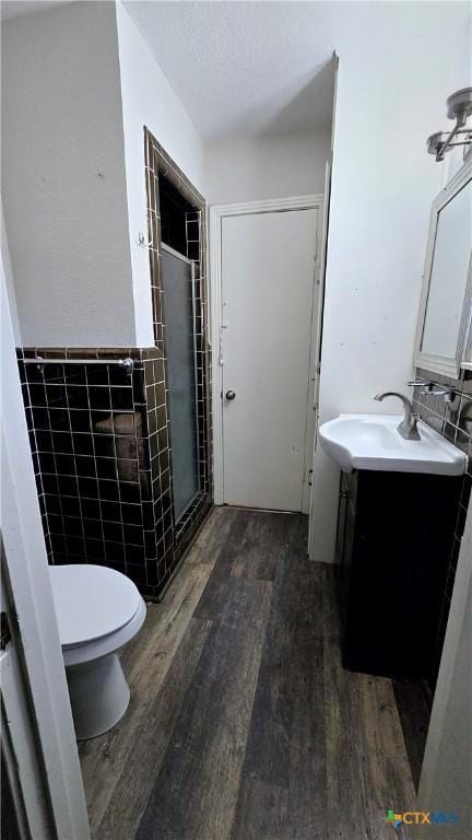 bathroom with toilet, wood finished floors, vanity, tile walls, and a stall shower