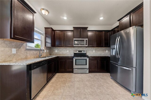 kitchen with tasteful backsplash, dark brown cabinets, light stone counters, a sink, and stainless steel appliances
