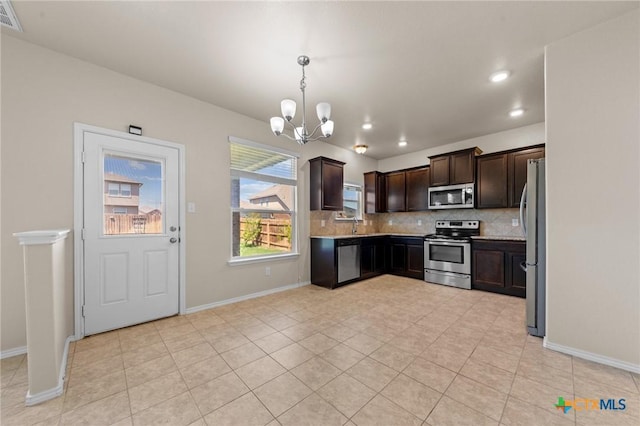 kitchen with light tile patterned floors, appliances with stainless steel finishes, a chandelier, dark brown cabinets, and decorative backsplash