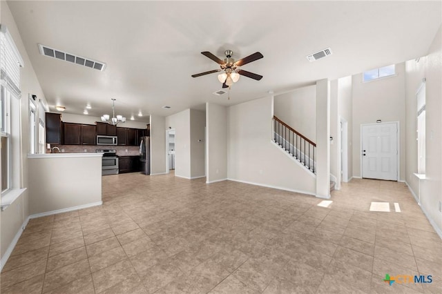 unfurnished living room featuring ceiling fan with notable chandelier, baseboards, visible vents, and stairs