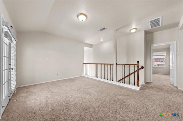 carpeted empty room featuring visible vents, baseboards, and lofted ceiling