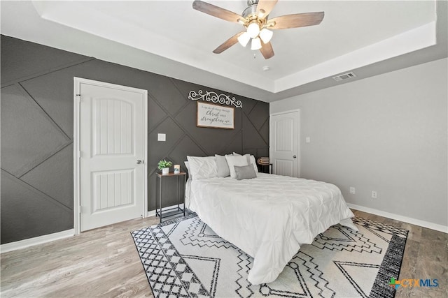 1110 Twin Deer Ln, Canyon Lake, TX 78133 - bedroom featuring a tray ceiling, light wood-type flooring, an accent wall, and a ceiling fan