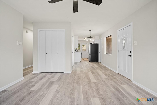 unfurnished living room with ceiling fan with notable chandelier and light hardwood / wood-style flooring