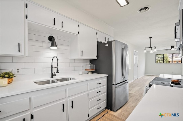 kitchen with sink, white cabinetry, light wood-type flooring, tasteful backsplash, and hanging light fixtures