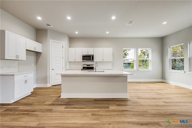 kitchen featuring a kitchen island with sink, light hardwood / wood-style flooring, stainless steel appliances, and white cabinets