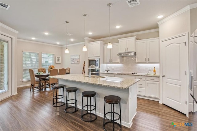 1330 Logan Blvd, Salado, TX 76571 - kitchen featuring under cabinet range hood, a breakfast bar, stainless steel microwave, white cabinetry, and recessed lighting