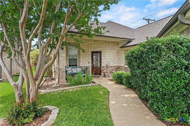 entrance to property featuring stone siding, a lawn, and roof with shingles