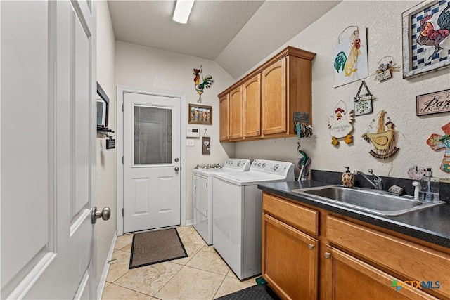 laundry area with cabinet space, a textured wall, washer and dryer, a sink, and light tile patterned flooring