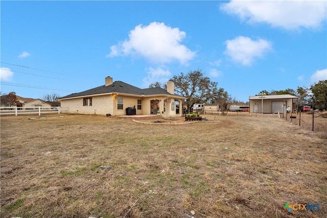 back of property featuring a detached garage, fence, a lawn, a chimney, and a patio area