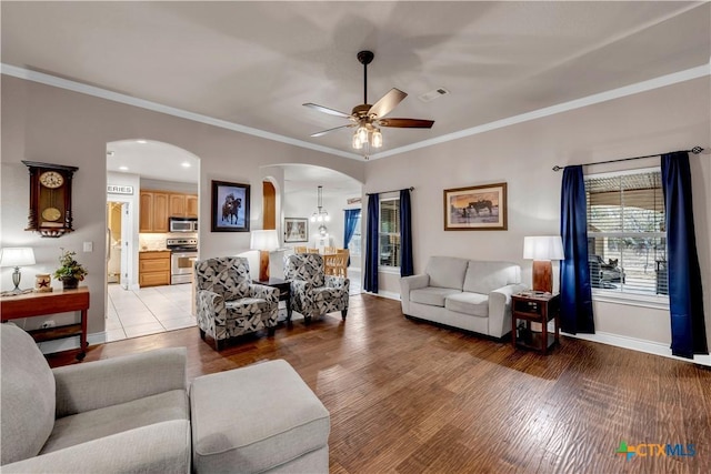 living room featuring visible vents, arched walkways, light wood-style floors, crown molding, and baseboards