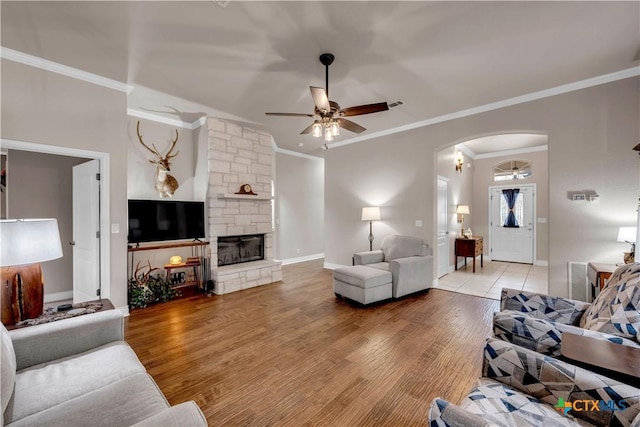 living room featuring baseboards, ceiling fan, light wood-style flooring, a fireplace, and arched walkways