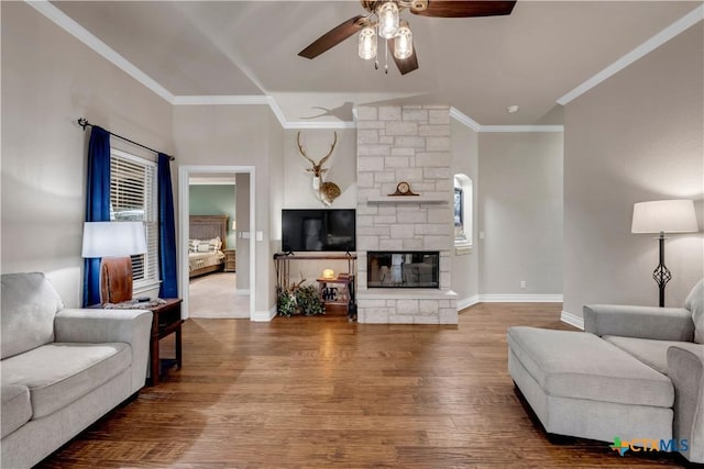 living room featuring baseboards, a stone fireplace, wood finished floors, and crown molding