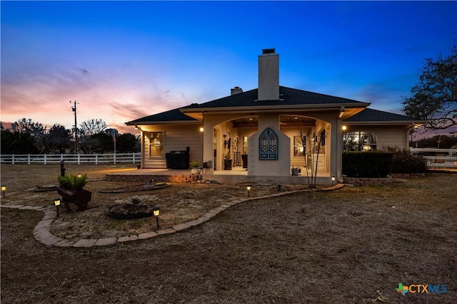 back of house at dusk featuring a patio, fence, and a chimney