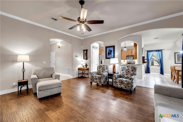 living area featuring visible vents, ceiling fan, baseboards, wood finished floors, and arched walkways