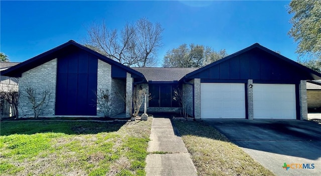 view of front of home with an attached garage, brick siding, driveway, board and batten siding, and a front yard