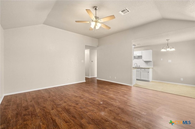 unfurnished living room featuring vaulted ceiling, ceiling fan with notable chandelier, wood finished floors, and visible vents