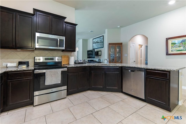 kitchen with stainless steel appliances, a peninsula, arched walkways, a sink, and light stone counters