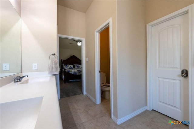 ensuite bathroom featuring toilet, tile patterned flooring, ceiling fan, baseboards, and double vanity