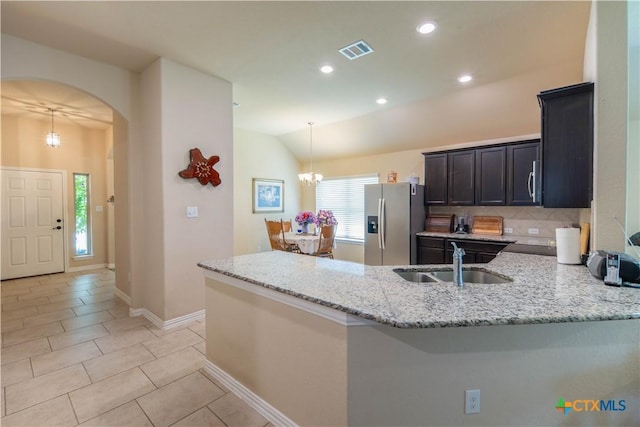 kitchen featuring stainless steel fridge, a sink, a chandelier, light stone counters, and a peninsula